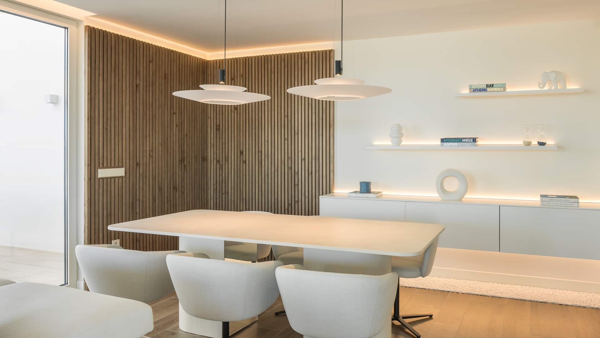 Comedor con lámparas suspendidas y pared de madera con perfil lineal LED perimetral, proyecto Inspira Design y JISO