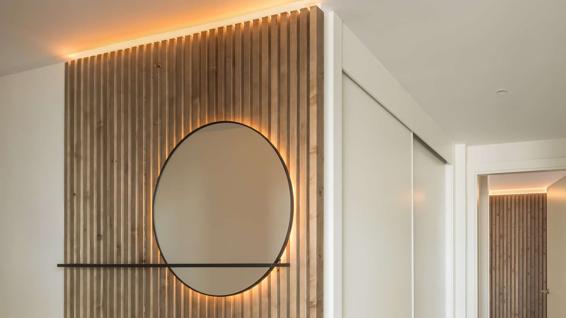 Espejo circular con retroiluminación LED integrada en panel de madera ranurada, iluminación JISO